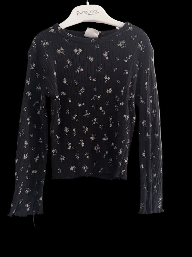 A black long-sleeve ribbed knit top with a small beige floral pattern, hanging on a white hanger labeled 'purebaby' against a white wall.