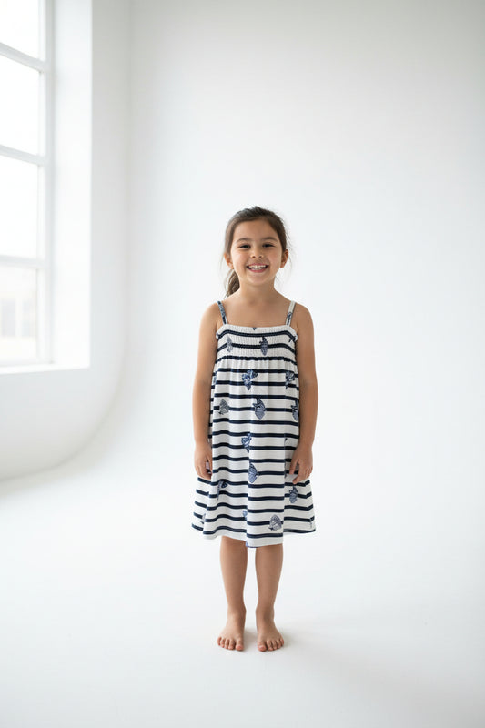 A sleeveless striped sundress with thin shoulder straps, featuring navy blue horizontal stripes and scattered blue floral motifs on a white background, hanging on a white plastic hanger against a plain gray wall.
