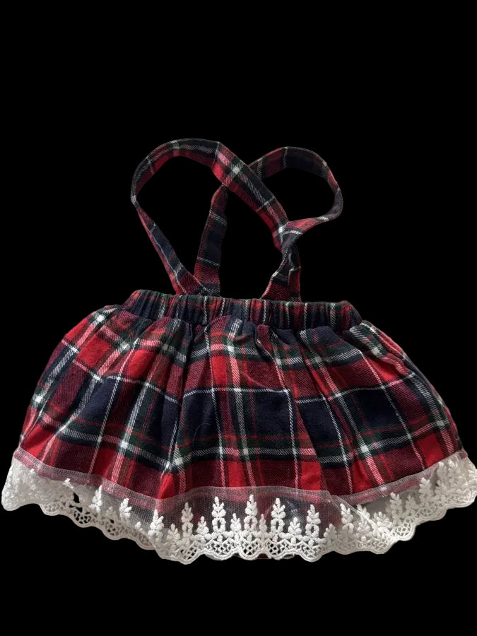 A small plaid shoulder bag with red, navy, and white tartan pattern, featuring double shoulder straps and a white lace trim along the bottom edge, laid flat on a light beige fabric background.