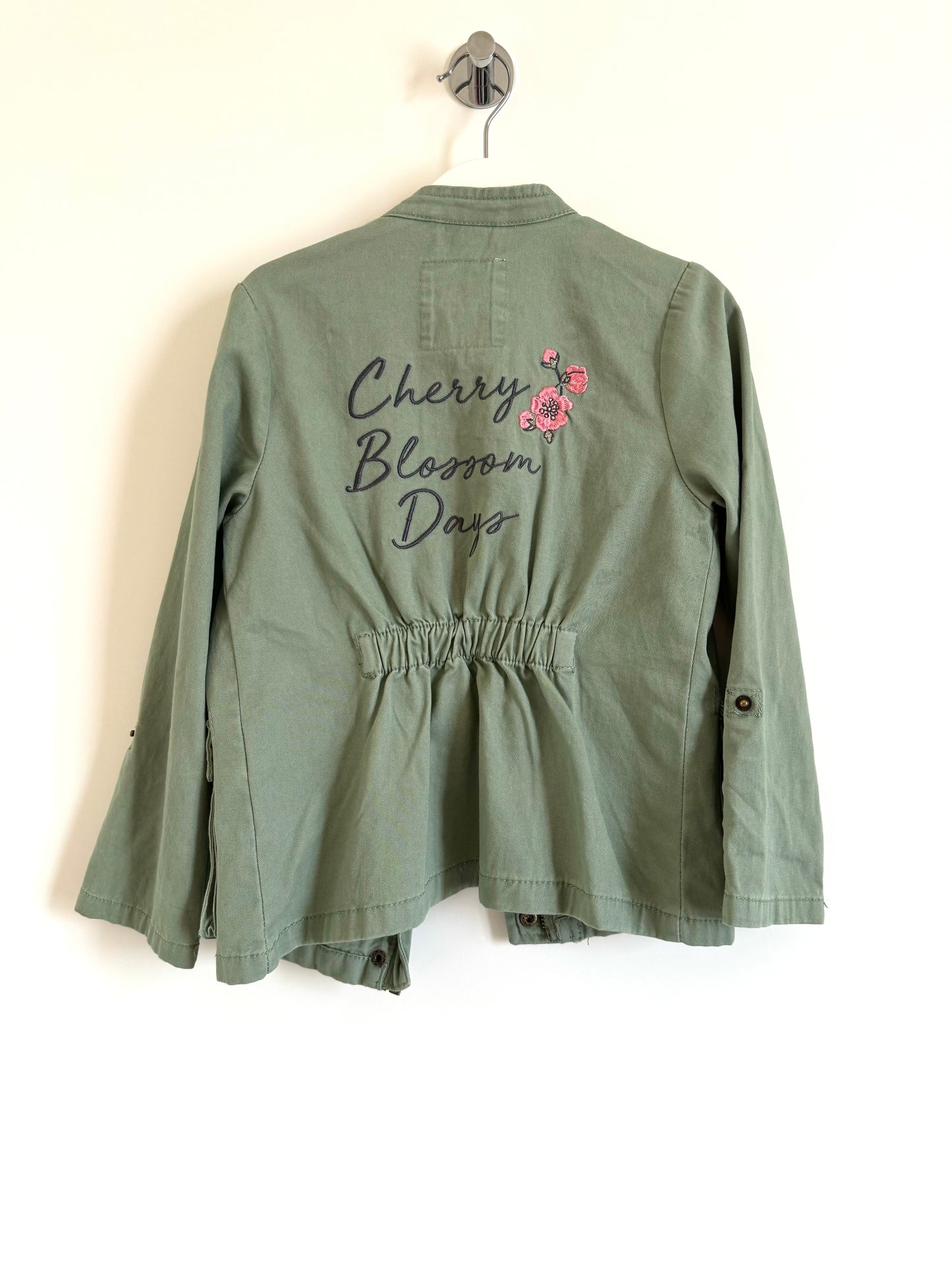 A khaki green jacket for girls with 'Cherry Blossom Day' text and a floral emblem on the back.
