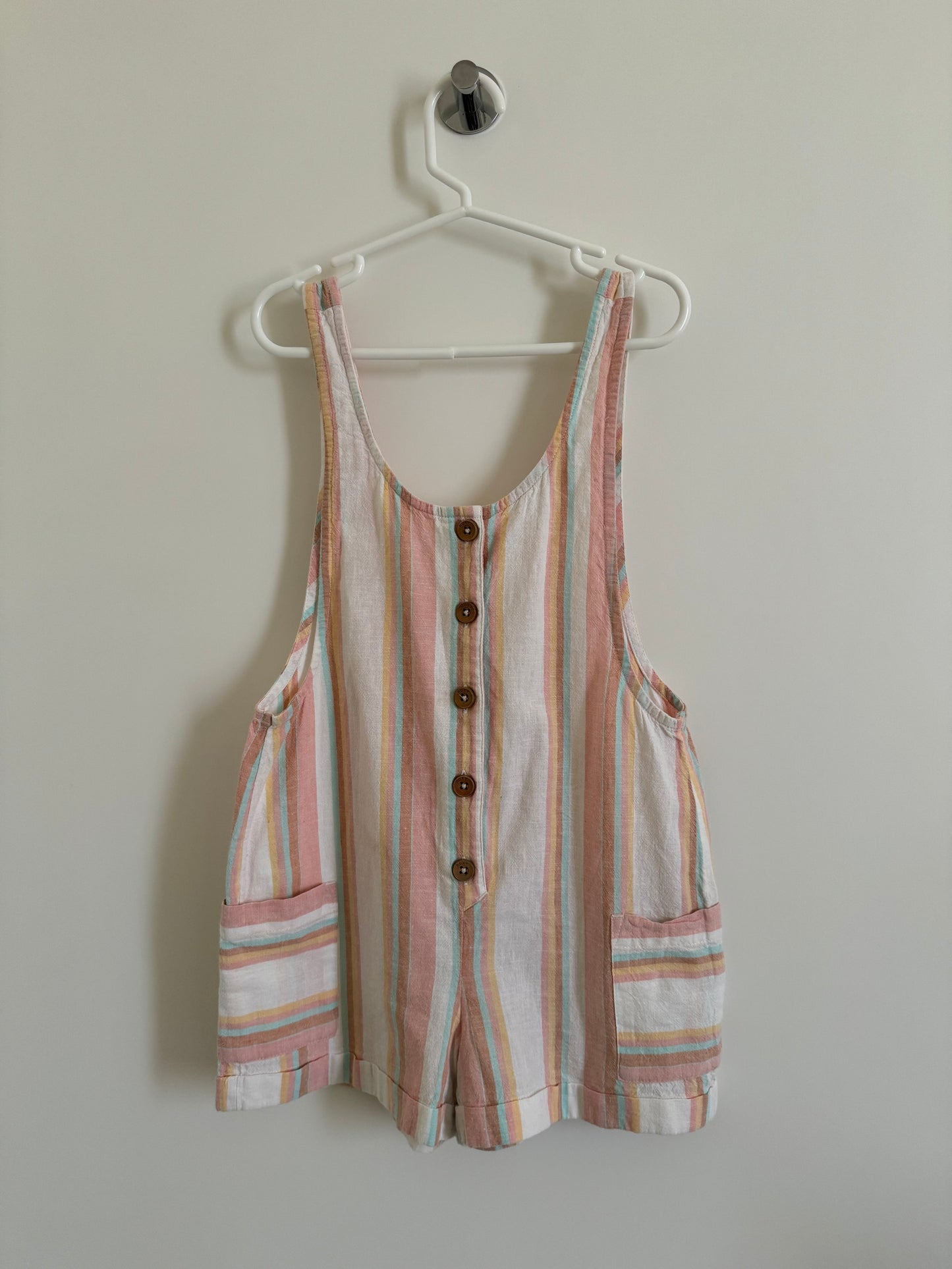 A pink and white striped sleeveless top for children hanging on a white hanger against a white wall.