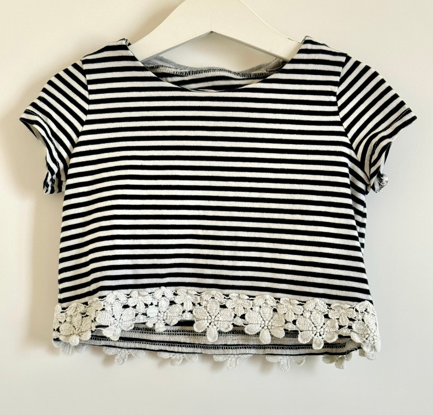 A short sleeved, cropped top with black and white stripes, featuring a lace-up front and white lace detailing on the sleeves.