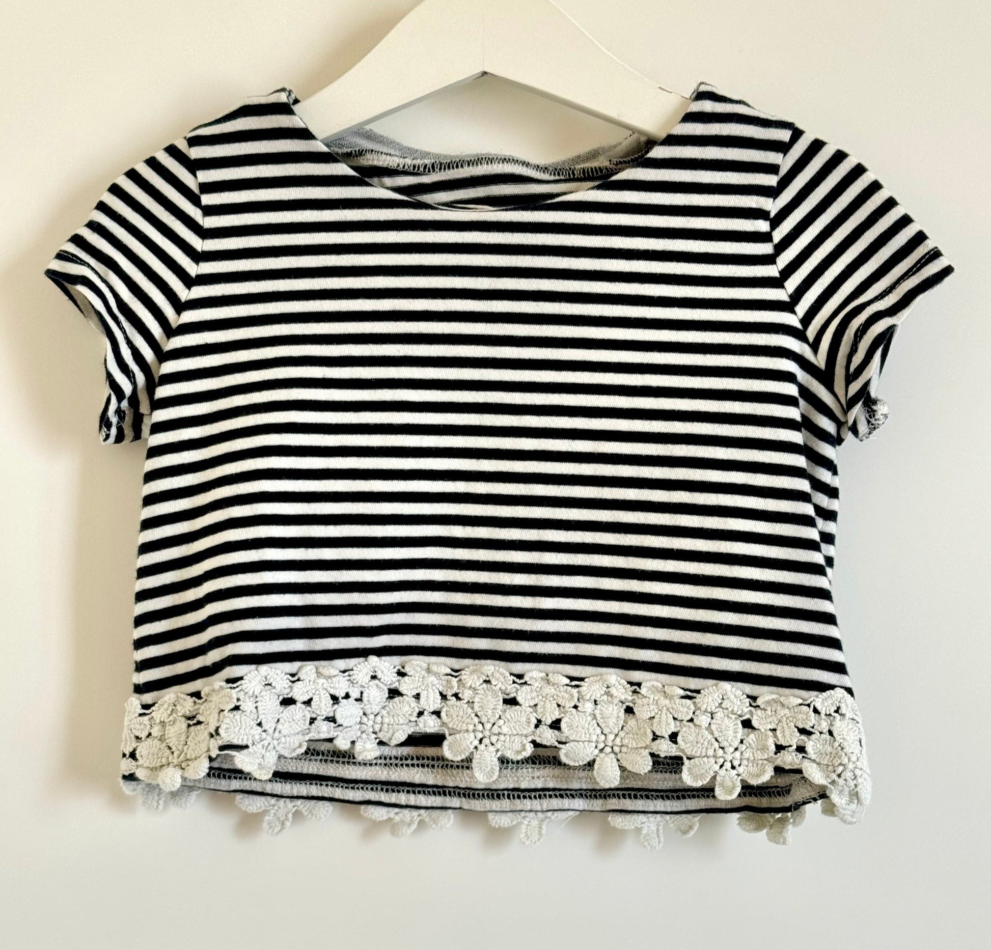 A short sleeved, cropped top with black and white stripes, featuring a lace-up front and white lace detailing on the sleeves.